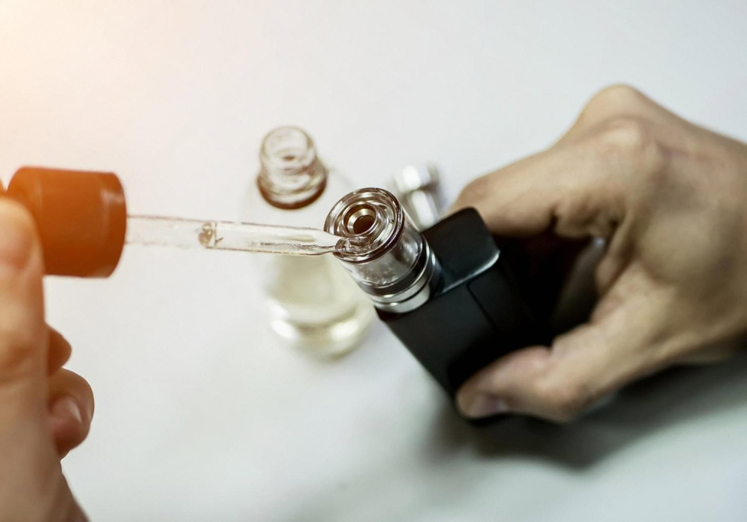 Dropper filling a vape tank with e-liquid on a white surface