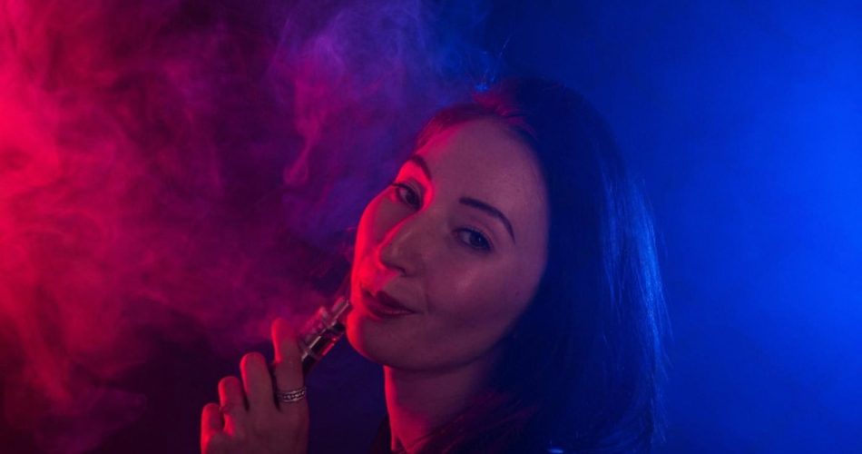 Woman exhaling vapour from an electronic cigarette under red and blue light